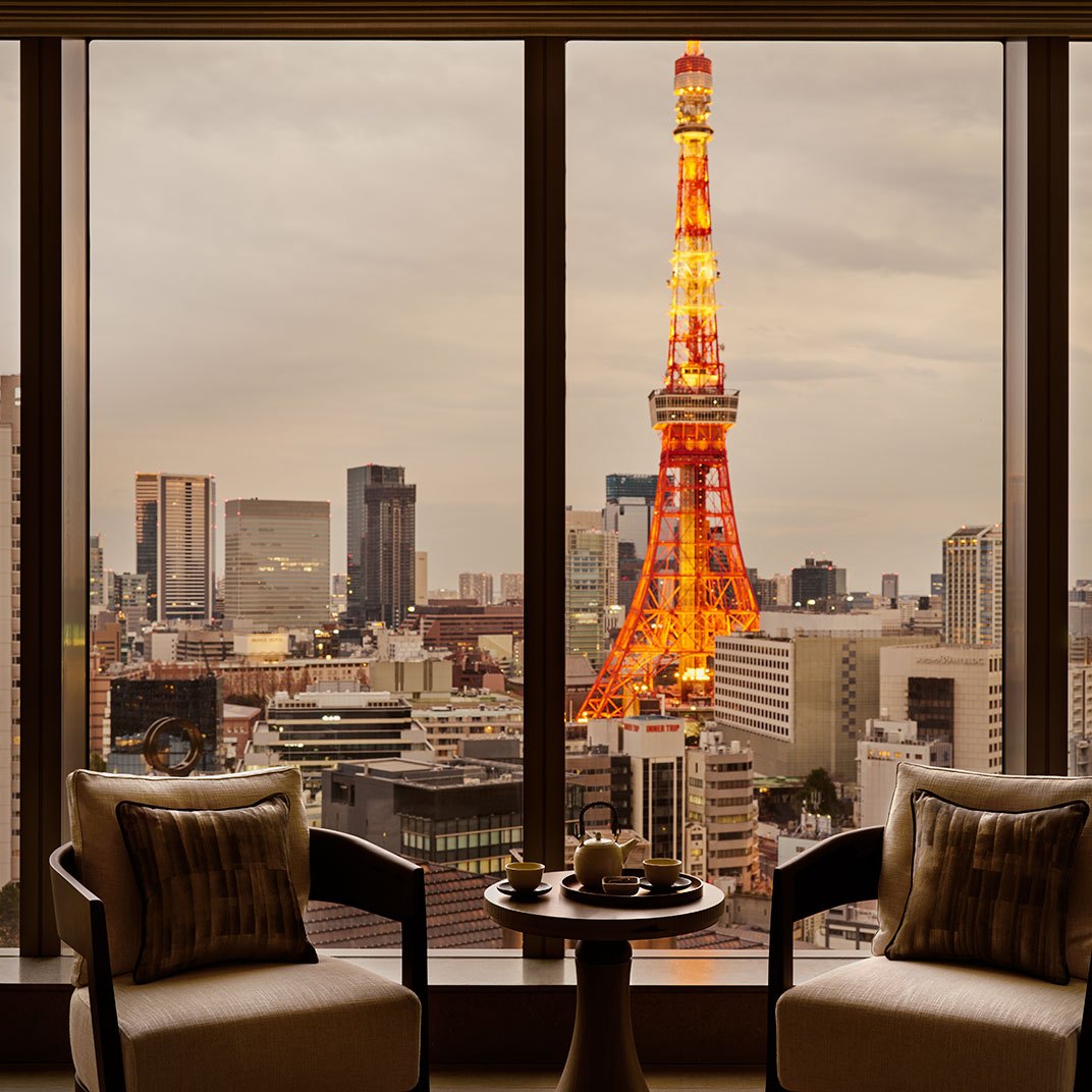 Two armchairs and a tea service before a window framing Tokyo Tower at dusk