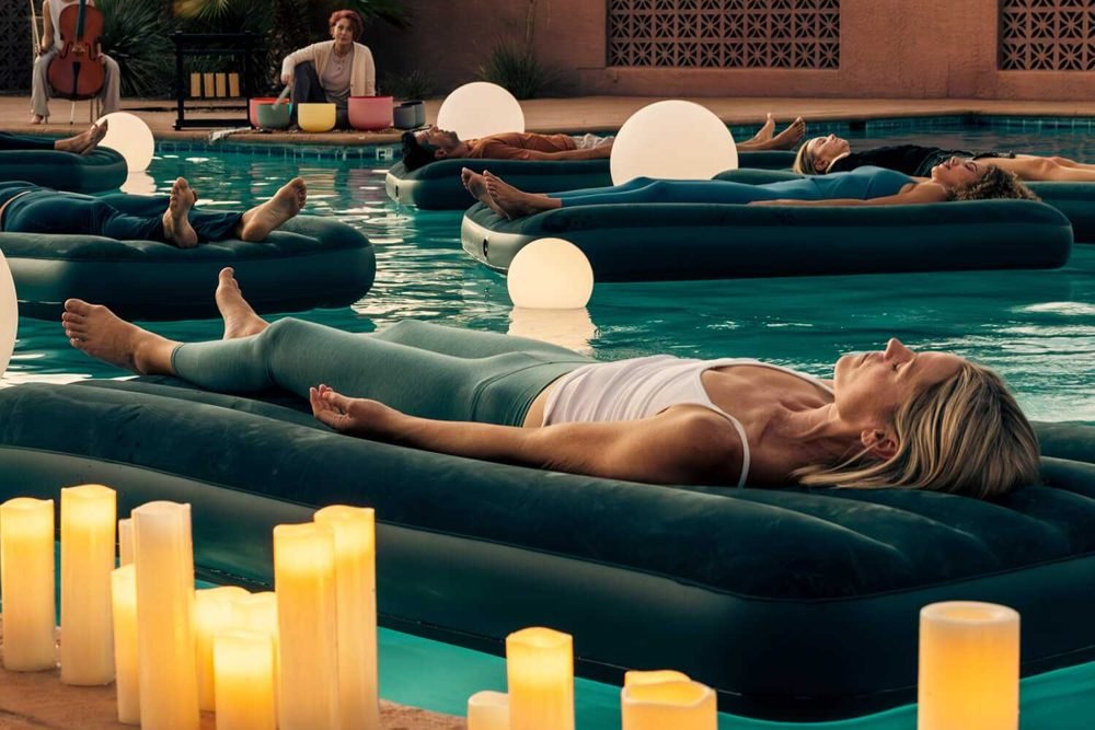 Guests floating on mats in a candlelit pool at a wellness retreat